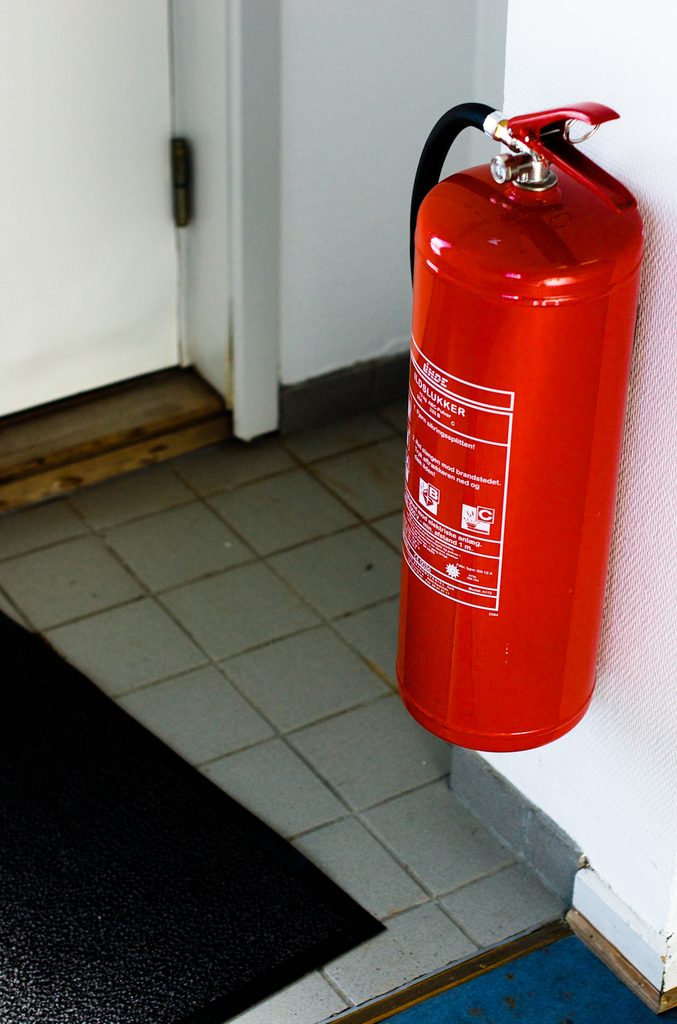 Red fire extinguisher mounted on a wall beside a doorway